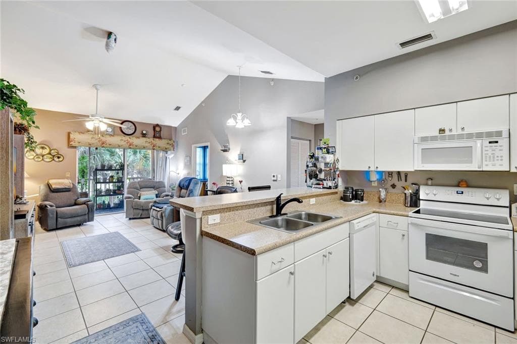 Kitchen with white appliances, white cabinets, hanging light fixtures, a peninsula, and a breakfast bar area