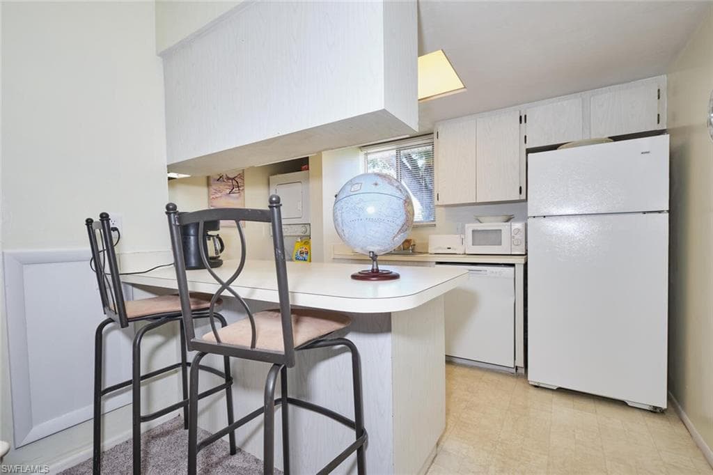 Kitchen featuring white appliances, light countertops, a kitchen bar, a peninsula, and light flooring