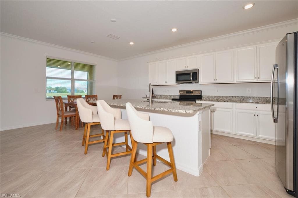 Kitchen with crown molding, white cabinets, appliances with stainless steel finishes, light stone countertops, and a breakfast bar area