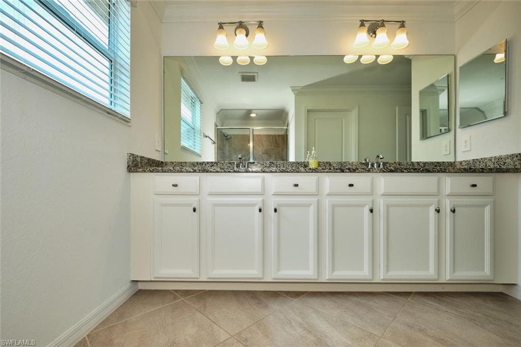 Full bath with a stall shower, ornamental molding, double vanity, and light tile patterned flooring