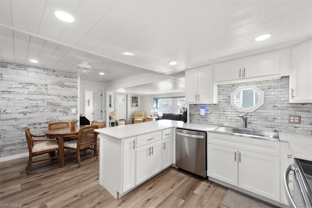 Kitchen featuring white cabinets, a peninsula, stainless steel appliances, wooden walls, and open floor plan