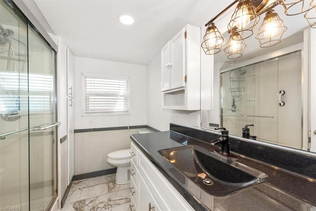Bathroom with vanity, a stall shower, light marble finish floors, a wainscoted wall, and a chandelier