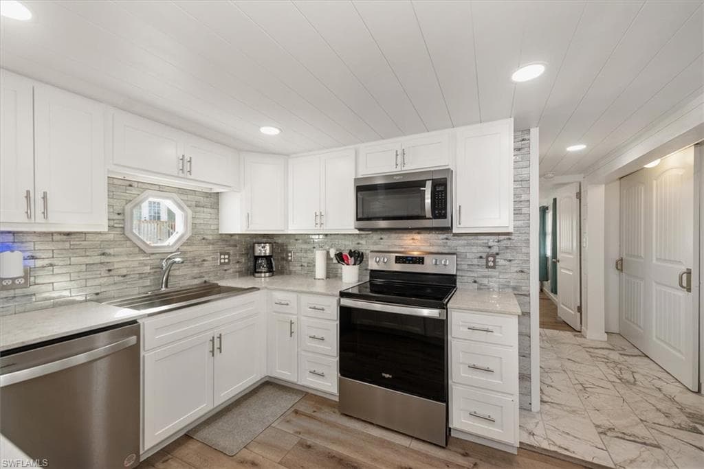 Kitchen featuring stainless steel appliances, white cabinets, recessed lighting, light stone countertops, and tasteful backsplash