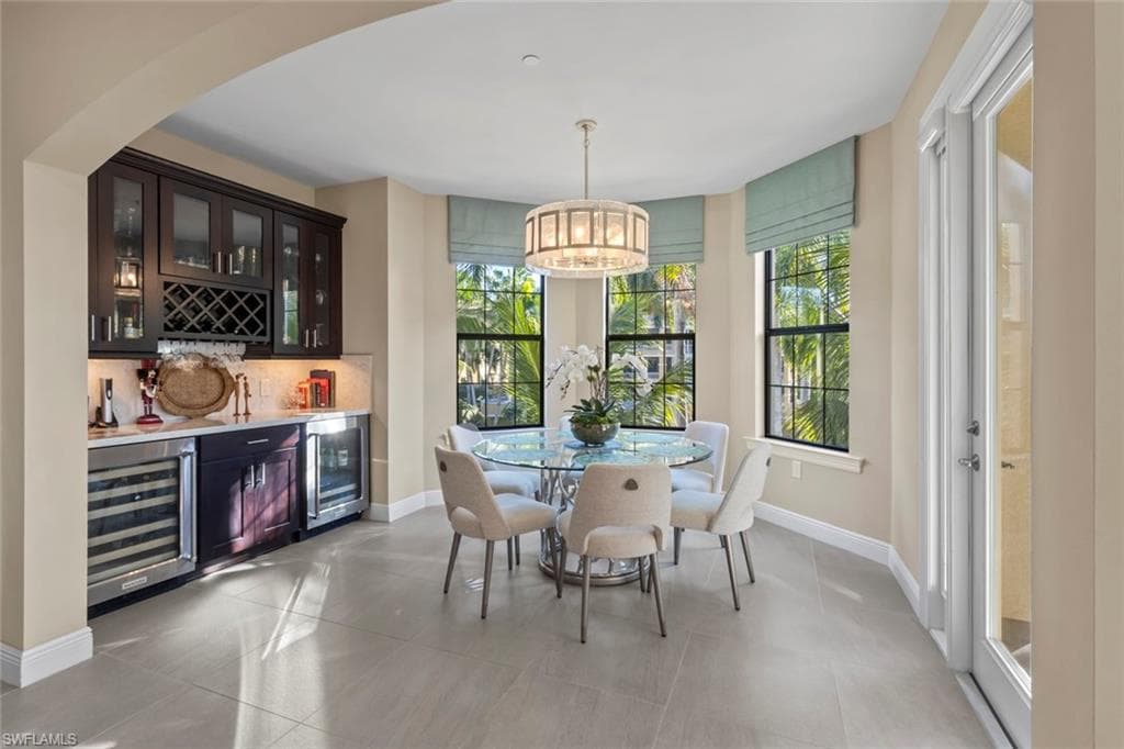 Indoor bar featuring glass insert cabinets, beverage cooler, decorative light fixtures, and light stone countertops
