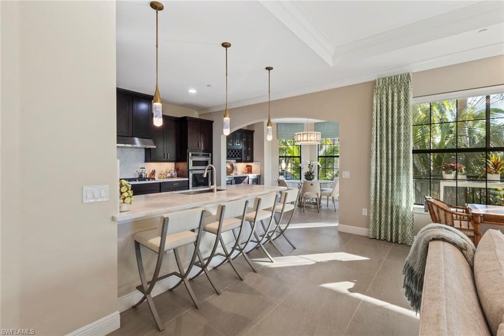 Kitchen with a breakfast bar, decorative light fixtures, light stone counters, ornamental molding, and stainless steel double oven