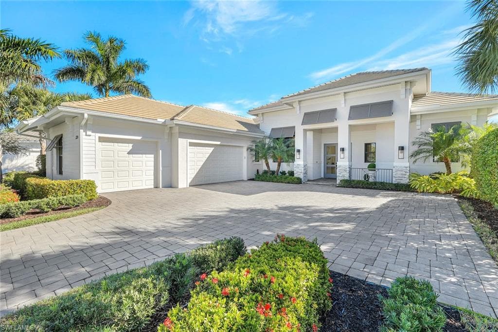 British West Indies house with decorative driveway, a garage, a tile roof, and stucco siding