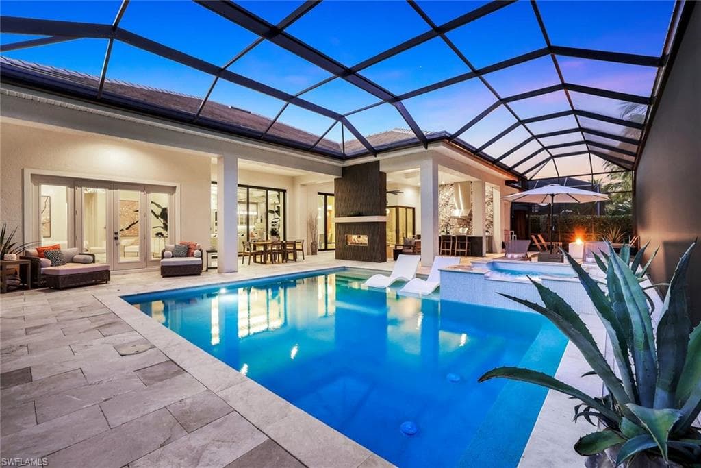 Pool at dusk with a sunroom, outdoor lounge area, glass enclosure, a patio, and a pool with connected hot tub