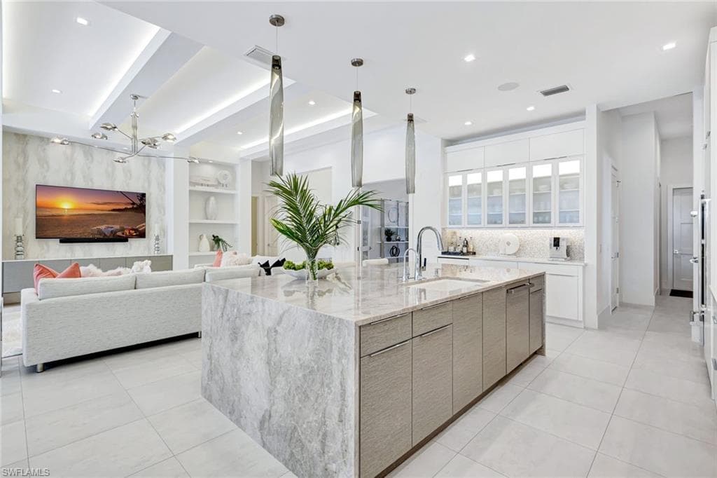Kitchen with built in features, an island with sink, light stone counters, beam ceiling, and recessed lighting