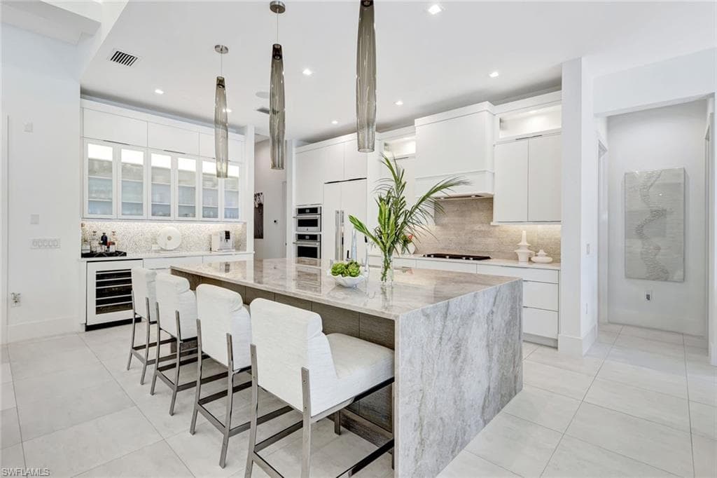 Kitchen with glass insert cabinets, white cabinets, a kitchen breakfast bar, light stone counters, and hanging light fixtures