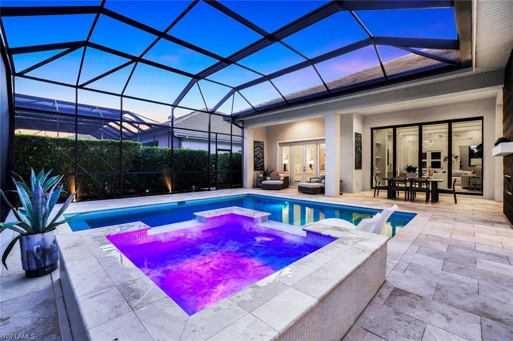 Pool at dusk with a sunroom, a lanai, a patio area, and a pool with connected hot tub