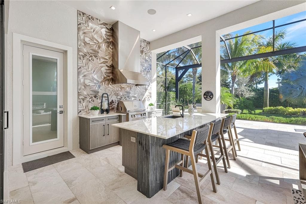 Kitchen featuring light stone counters, modern cabinets, a kitchen breakfast bar, wall chimney range hood, and a sunroom