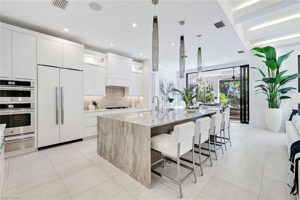 Kitchen with white cabinetry, modern cabinets, paneled built in refrigerator, decorative light fixtures, and light stone counters