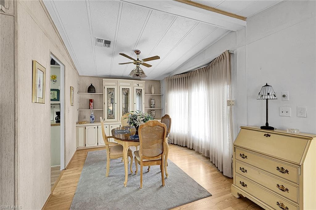 Dining space with light wood finished floors, a ceiling fan, vaulted ceiling with beams, and built in shelves