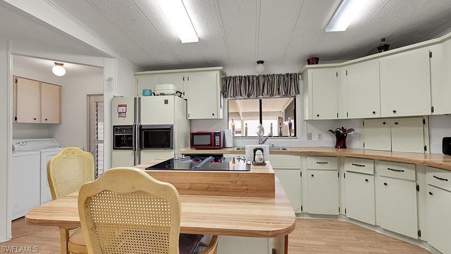 Kitchen featuring white fridge with ice dispenser, light wood-style floors, washing machine and clothes dryer, butcher block counters, and black electric stovetop