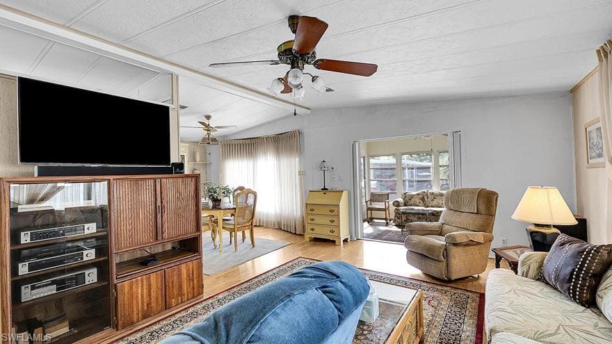 Living area with ceiling fan, wood finished floors, and vaulted ceiling with beams