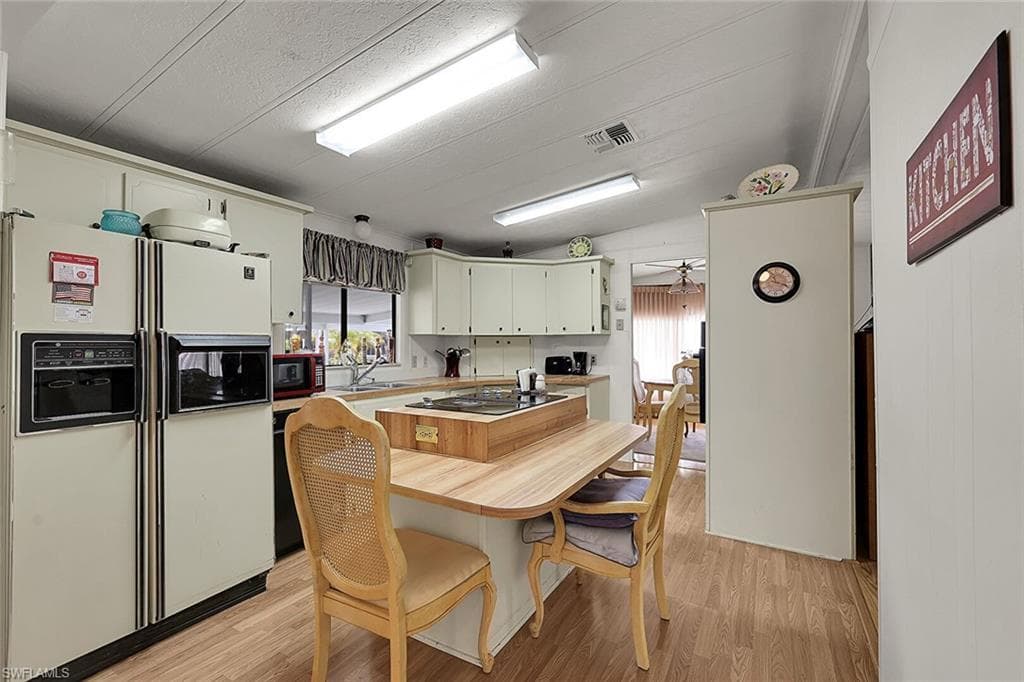 Kitchen with white refrigerator with ice dispenser, light wood-type flooring, a kitchen island, lofted ceiling, and ceiling fan