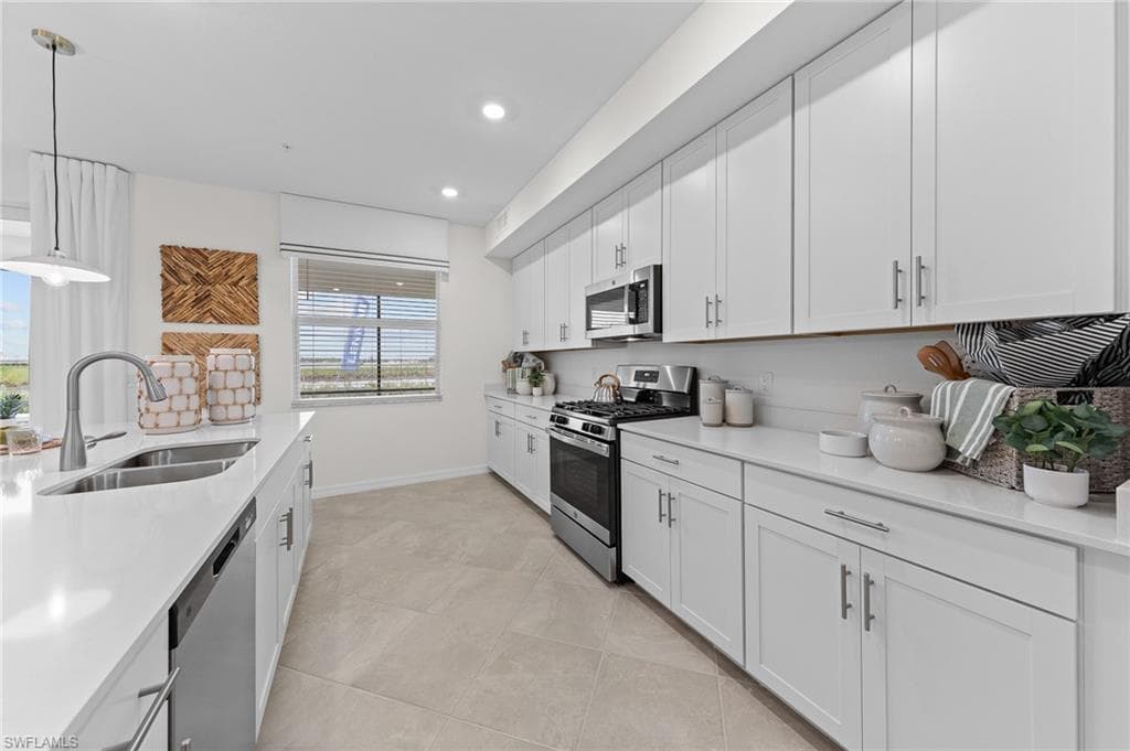 Kitchen featuring hanging light fixtures, white cabinets, appliances with stainless steel finishes, light stone counters, and recessed lighting