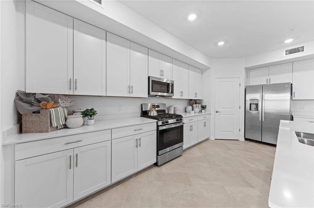 Kitchen featuring stainless steel appliances, white cabinets, light stone countertops, and recessed lighting