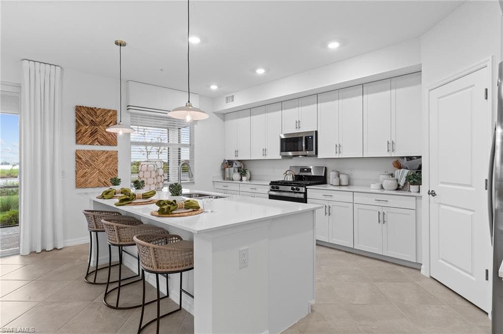 Kitchen with stainless steel appliances, a kitchen island with sink, a breakfast bar, white cabinets, and recessed lighting