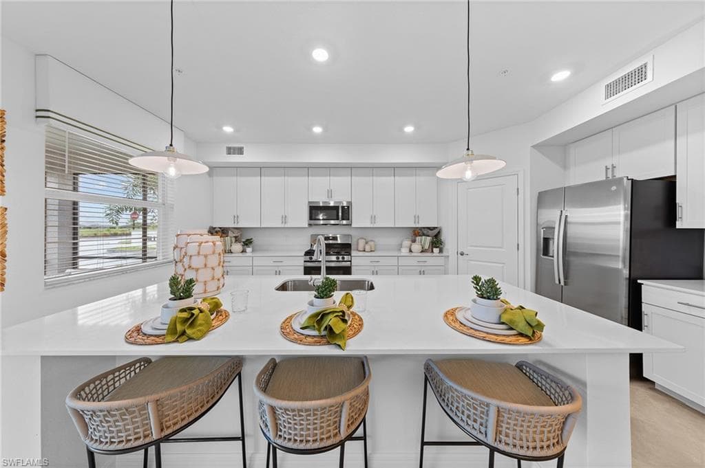 Kitchen with a kitchen bar, white cabinets, hanging light fixtures, and recessed lighting