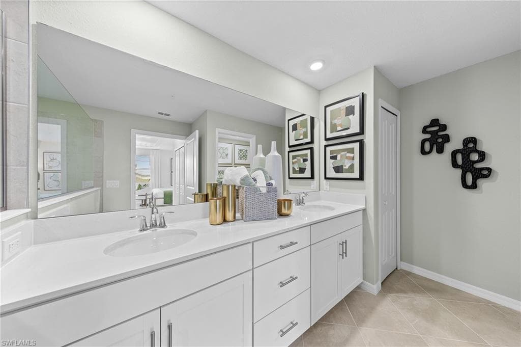 Ensuite bathroom with double vanity, light tile patterned floors, and a closet