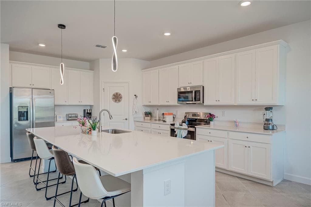 Kitchen with white cabinetry, appliances with stainless steel finishes, a breakfast bar area, a large island with sink, and recessed lighting