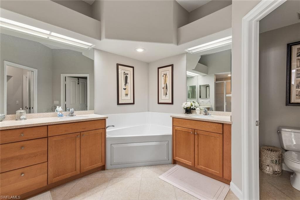 Full bathroom featuring a garden tub, light tile patterned floors, two vanities, a stall shower, and recessed lighting