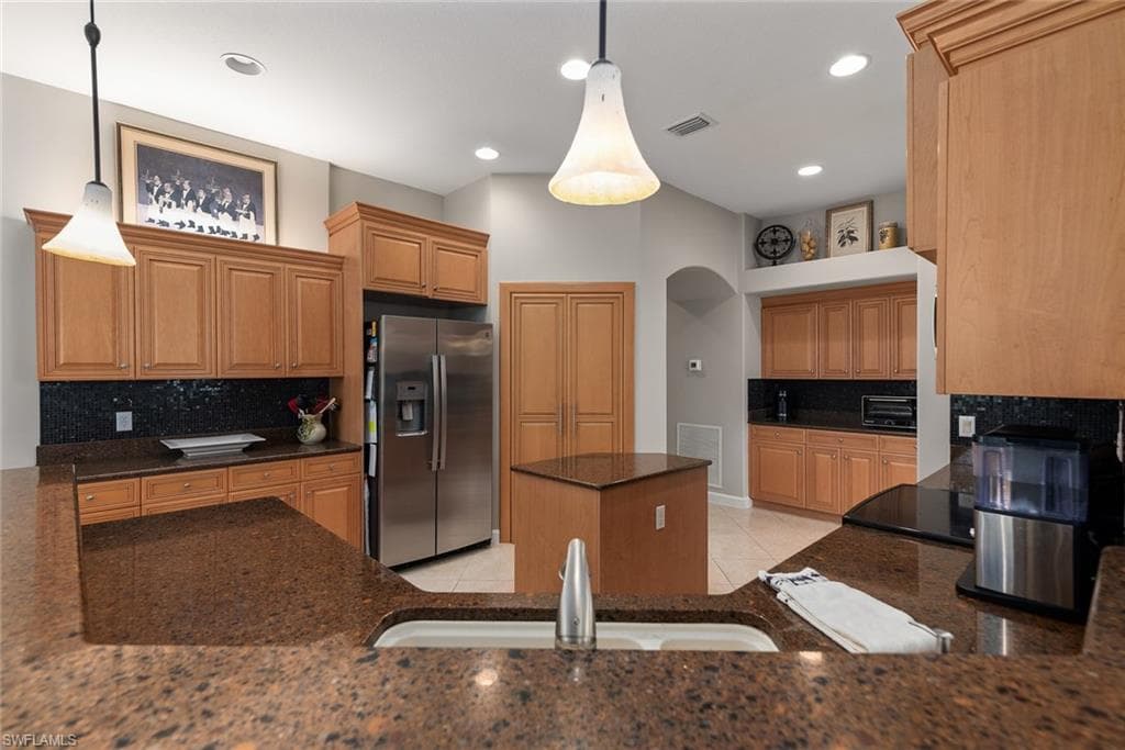 Kitchen featuring tasteful backsplash, stainless steel fridge, a center island, dark stone countertops, and hanging light fixtures