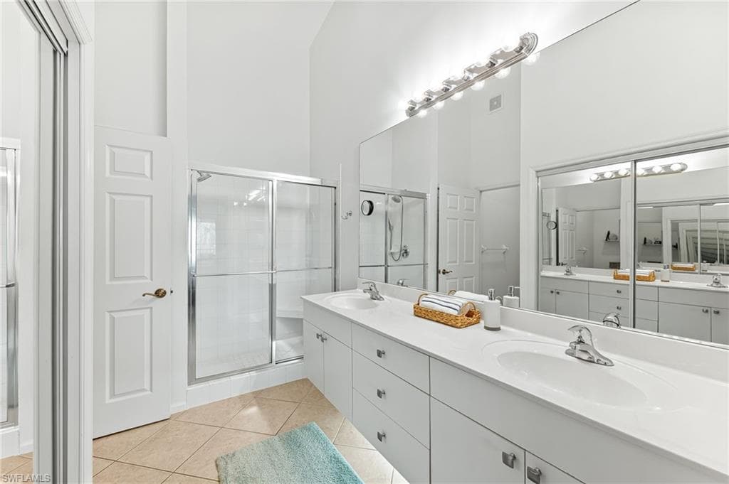 Bathroom featuring double vanity, a shower stall, a towering ceiling, and light tile patterned floors