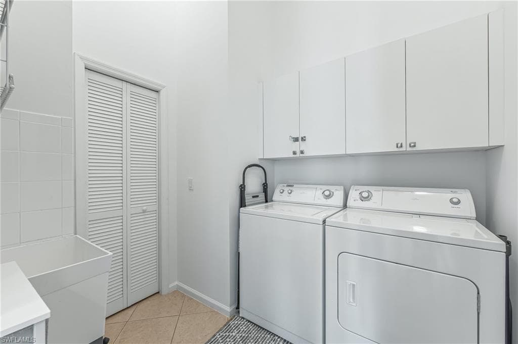 Laundry area with light tile patterned flooring, washing machine and dryer, and cabinet space