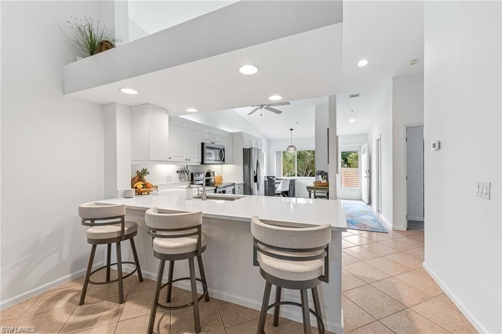 Kitchen featuring a peninsula, a breakfast bar, white cabinets, light tile patterned floors, and recessed lighting
