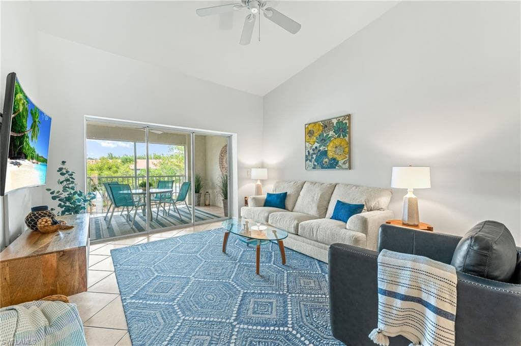 Living area with high vaulted ceiling, light tile patterned flooring, and ceiling fan
