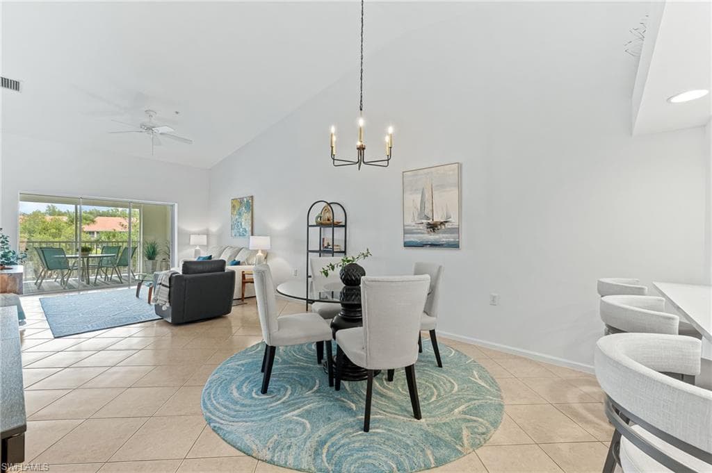 Dining area featuring high vaulted ceiling, ceiling fan, a chandelier, and light tile patterned flooring