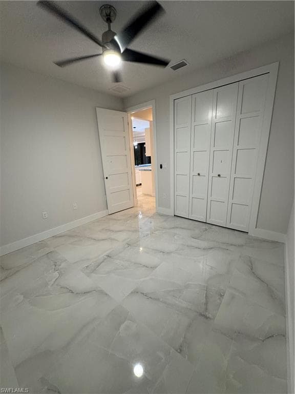 Unfurnished bedroom featuring light marble finish floors, a closet, and ceiling fan