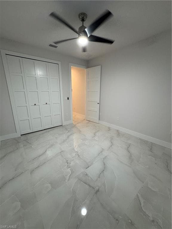 Unfurnished bedroom with light marble finish flooring, a closet, and a ceiling fan