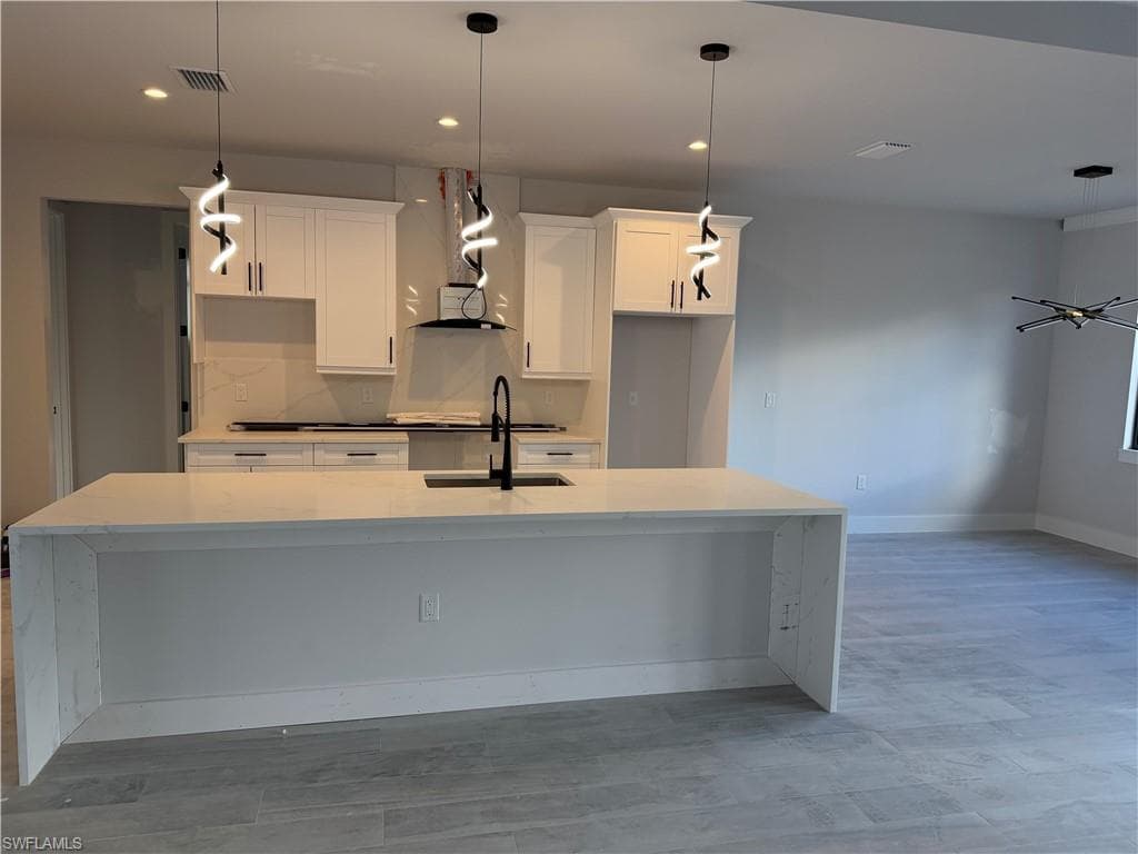 Kitchen featuring light stone countertops, white cabinetry, pendant lighting, and recessed lighting