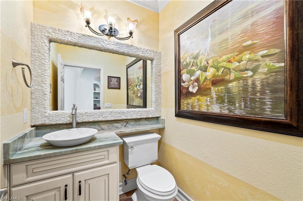 Bathroom with a textured wall, vanity, ornamental molding, and a chandelier