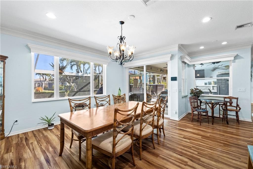 Dining space with wood finished floors, a chandelier, and ornamental molding