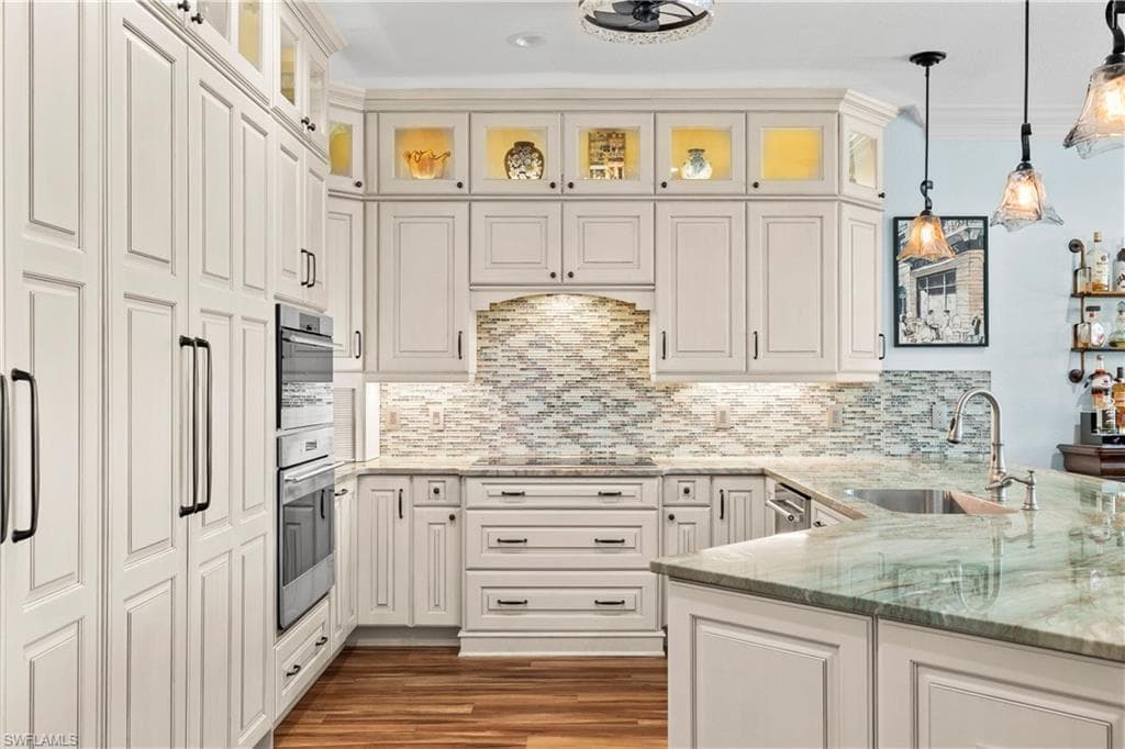 Kitchen featuring light stone countertops, pendant lighting, ornamental molding, glass insert cabinets, and dark wood-style flooring