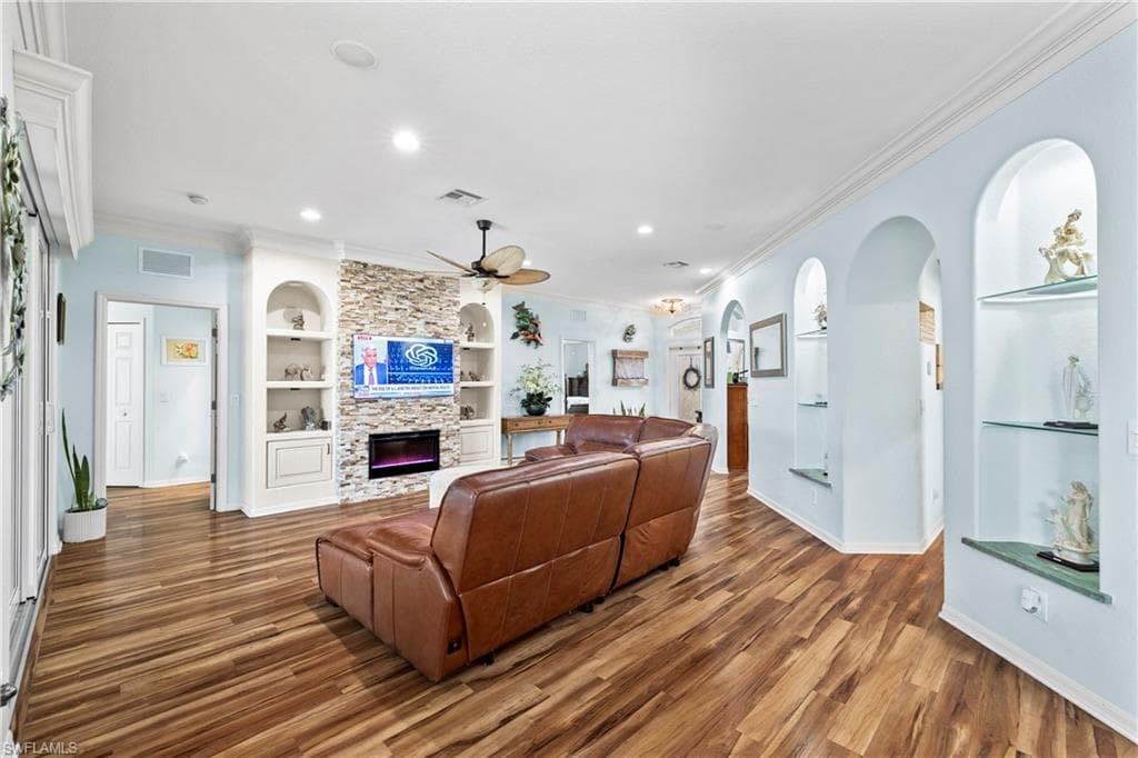Living area featuring built in features, crown molding, a fireplace, a ceiling fan, and wood finished floors