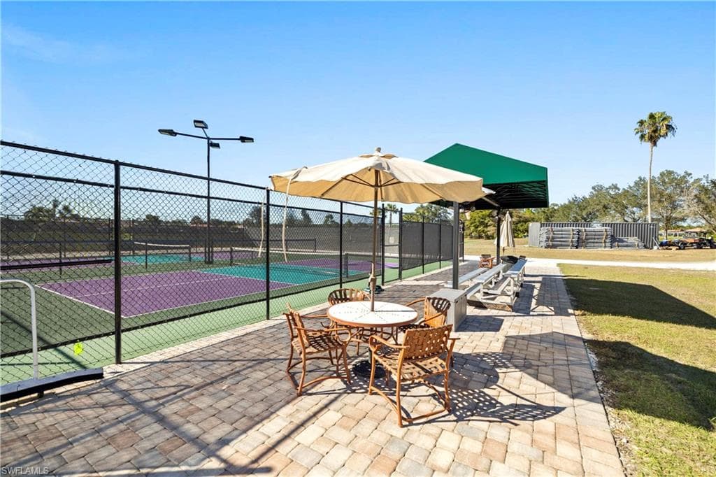 View of tennis court with a patio area and outdoor dining space
