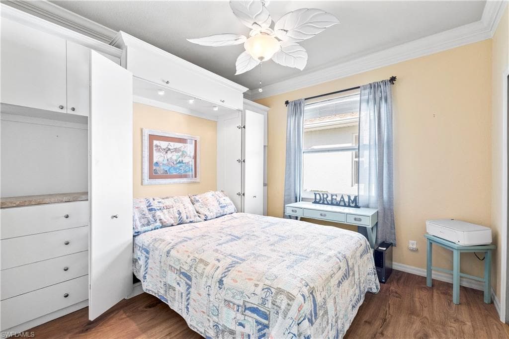 Bedroom with dark wood finished floors, ornamental molding, and ceiling fan