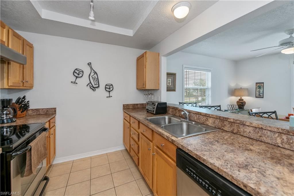 Kitchen featuring stainless steel appliances, sink, a raised ceiling, ceiling fan, and light tile patterned floors