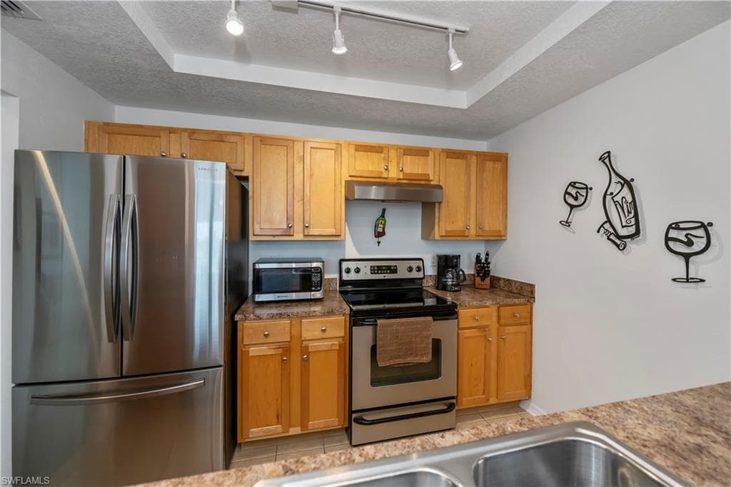 Kitchen featuring a textured ceiling, stainless steel appliances, sink, light tile patterned flooring, and a tray ceiling