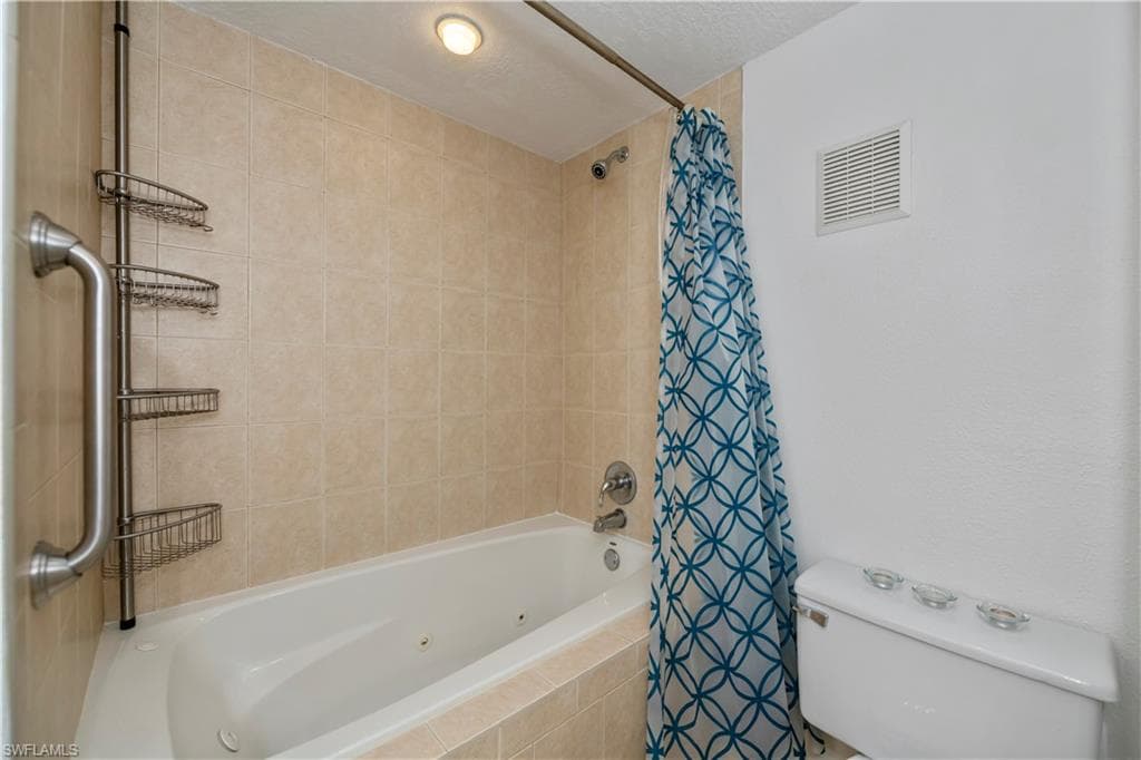 Bathroom featuring toilet, a textured ceiling, and shower / bathtub combination with curtain