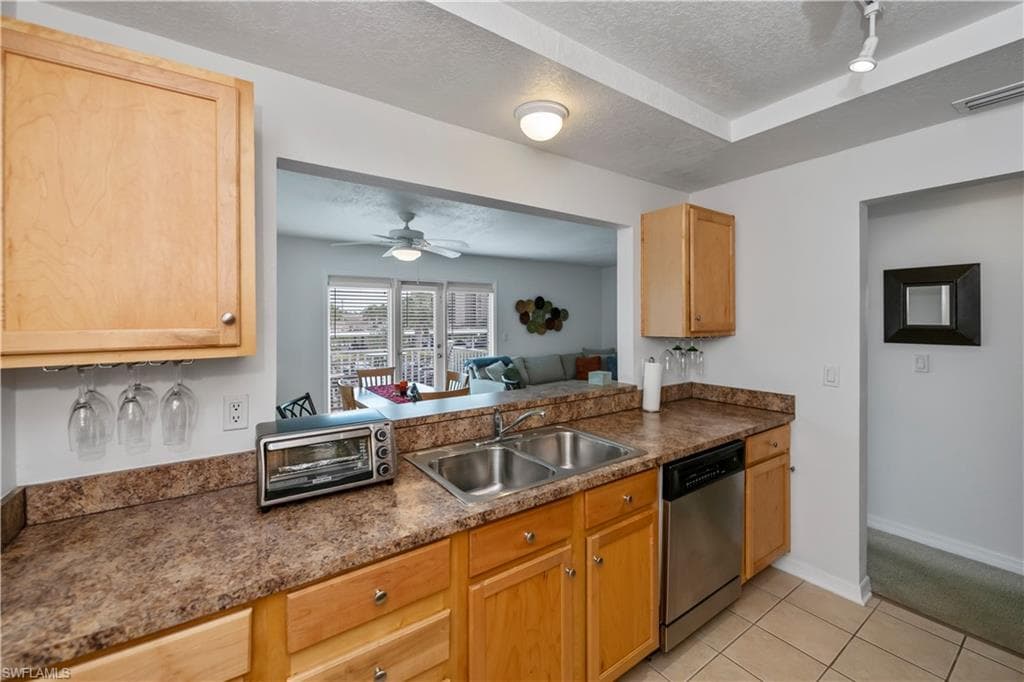 Kitchen featuring ceiling fan, stainless steel dishwasher, sink, light tile patterned flooring, and a textured ceiling