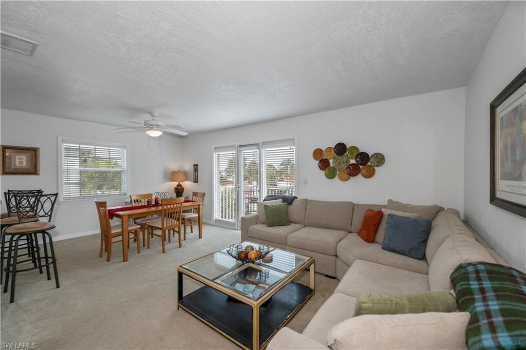Living room with ceiling fan, a textured ceiling, and light carpet