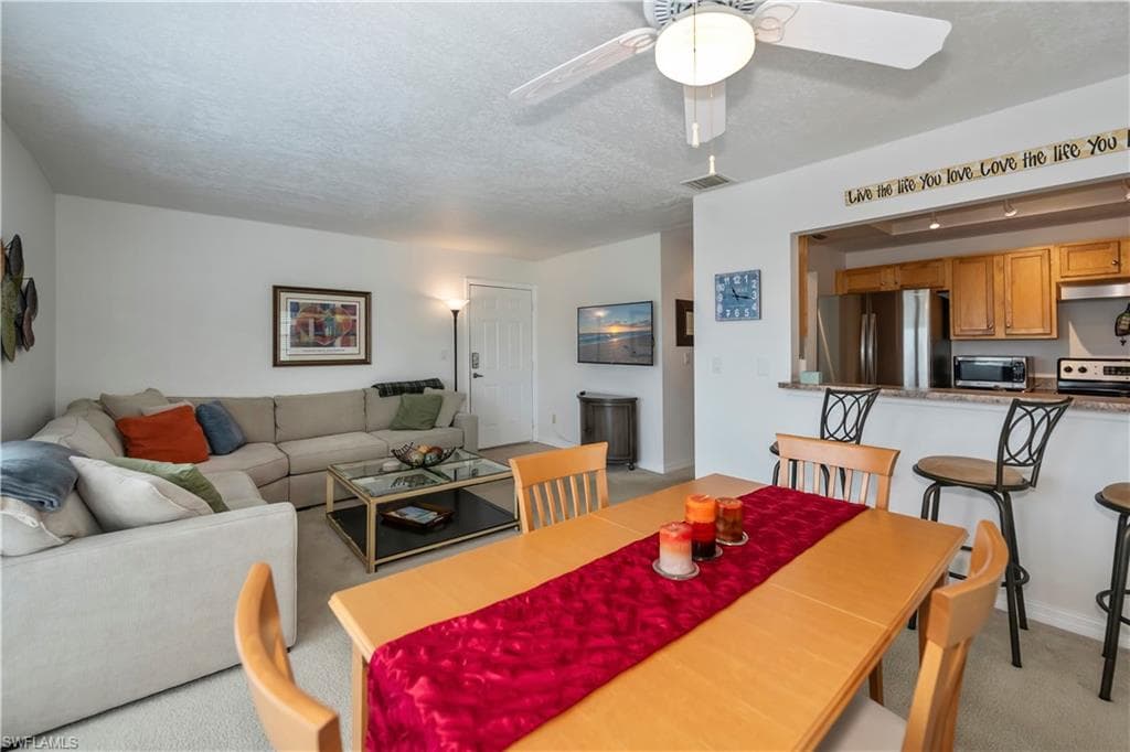 Dining room featuring ceiling fan, light carpet, and a textured ceiling