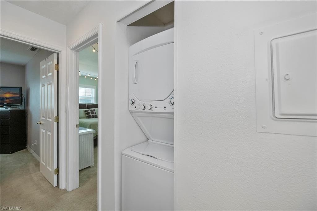 Clothes washing area featuring electric panel, stacked washer and clothes dryer, and light colored carpet