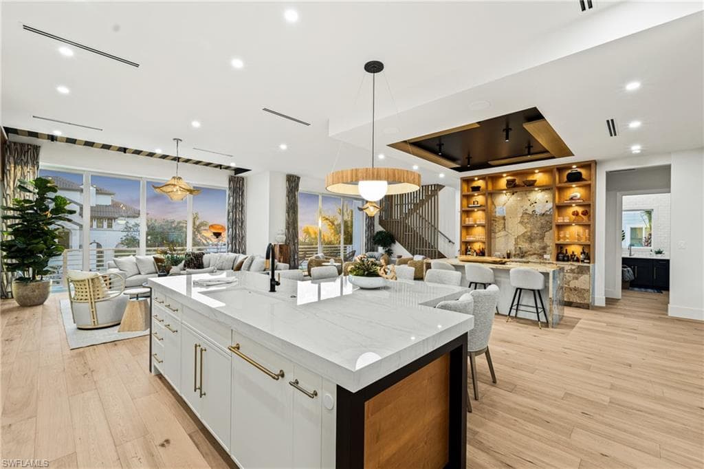 Kitchen with open floor plan, light stone countertops, light wood-type flooring, pendant lighting, and a tray ceiling